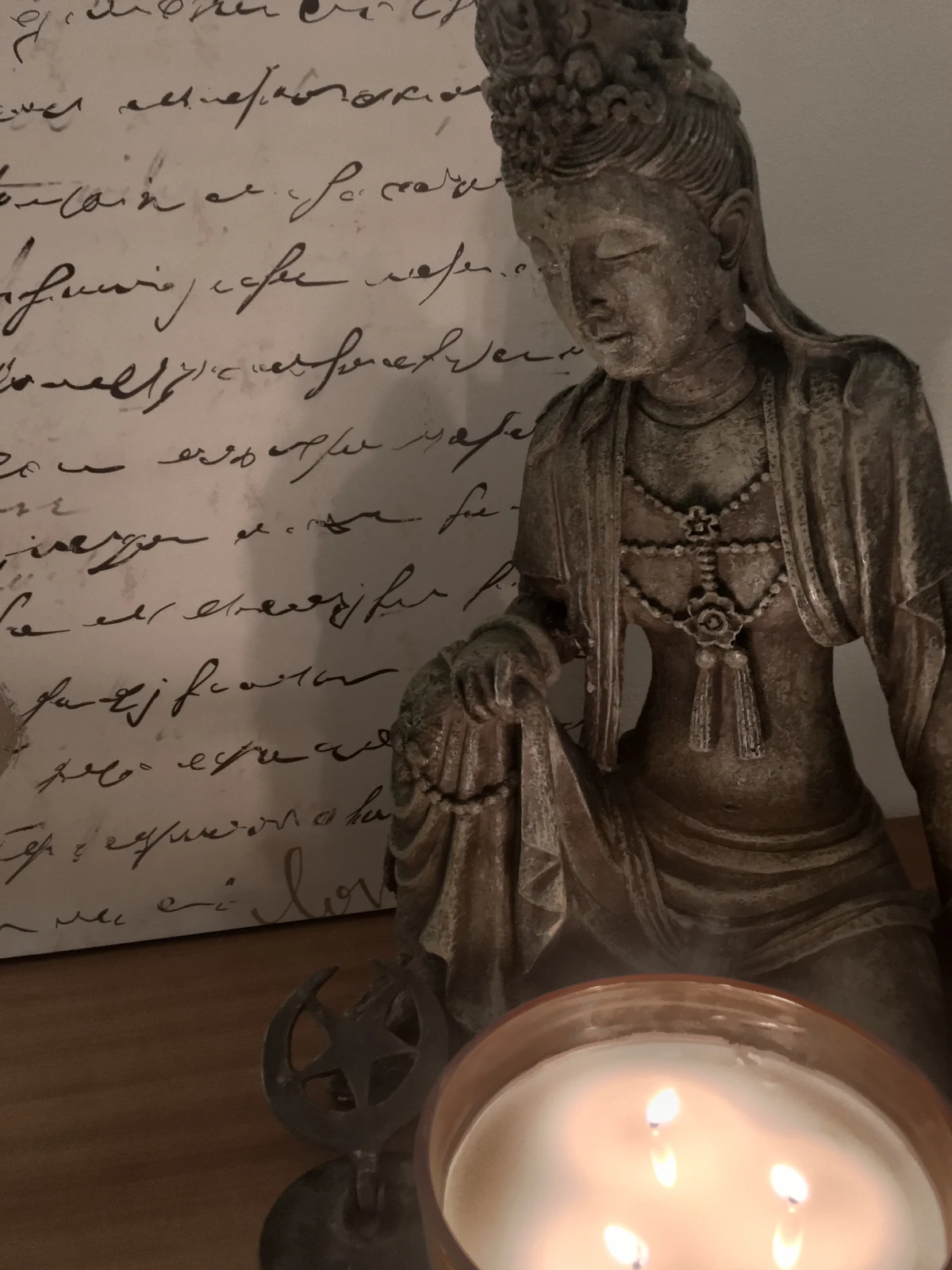 A Kuan Yin statue beside a lit candle and handwritten script